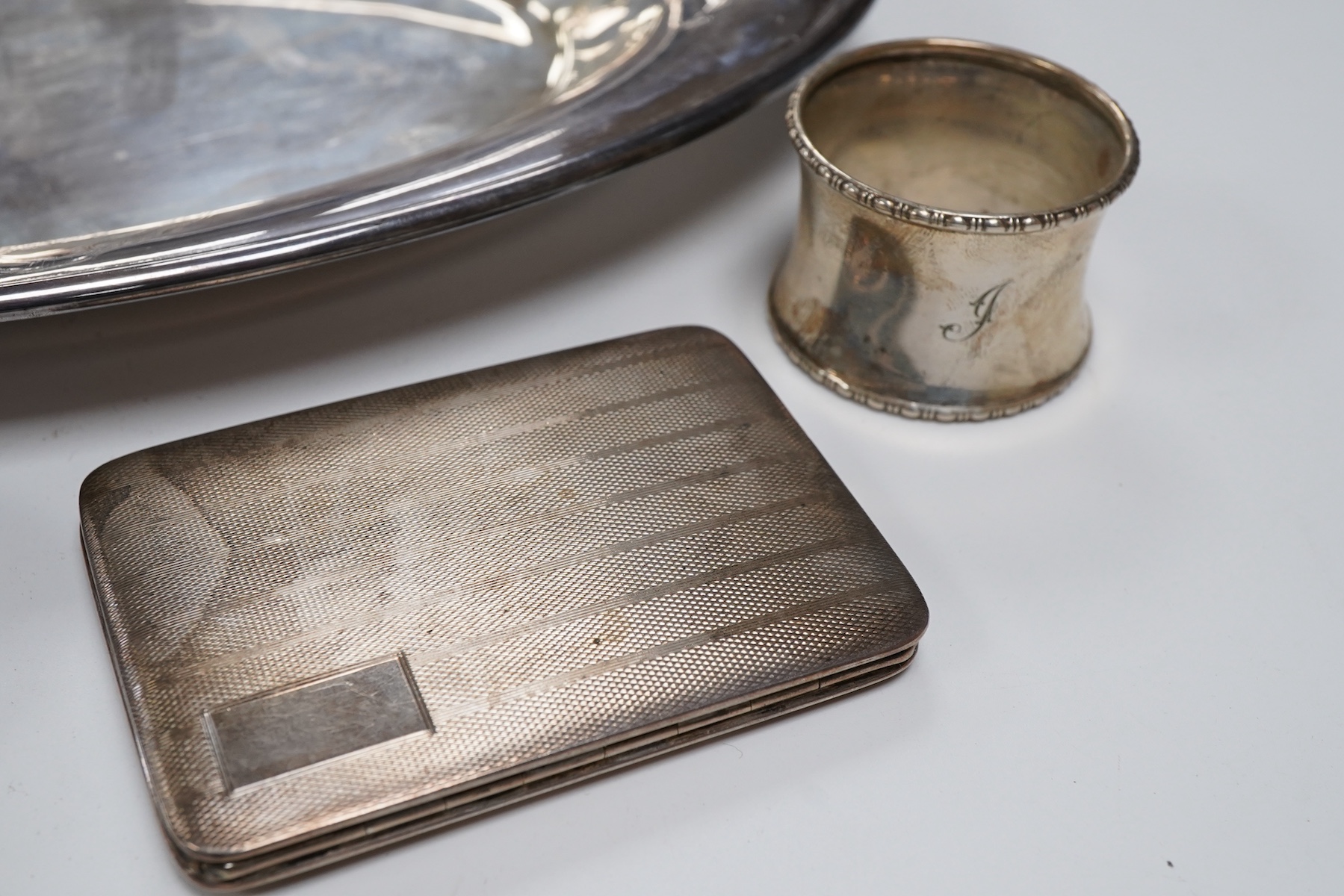 A Victorian silver bun salt, London, 1860, a later silver cigarette case, a silver napkin ring and pair of silver sugar tongs, together with a continental white metal serving spoon and a silver plated oval tray.